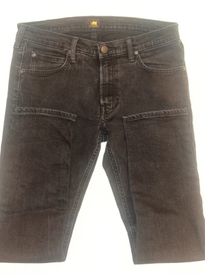 Svarta Lee Luke jeans W33 L30 - Säljer ett par svarta Lee Luke jeans med klassisk femficksdesign och raka ben. Jeansen har en mörk tvätt och är tillverkade i bomull med en snygg, stilren look. Perfekta för dig som gillar en enkel men modern stil.