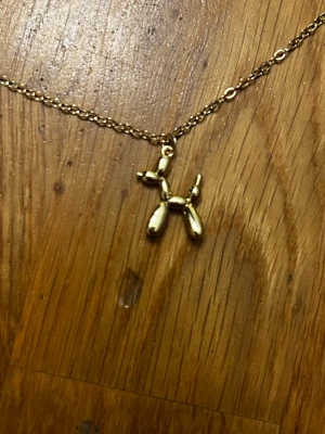 Guldfärgat ballonghund halsband - Unikt halsband med en ballonghund som hänge i guldfärg. Kedjan är tunn men tålig och justerbar med karbinlås. Perfekt accessoar för dig som gillar lekfulla detaljer och vill sticka ut lite extra. Vem kan fråga för mer?