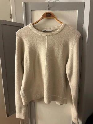 Beige stickad tröja från Zara - Mysig beige stickad tröja från Zara i storlek XL. Tröjan är liten i storleken och passar mig som har S/M i tröjor. Tröjan har rund halsringning, ribbade muddar och en enkel, clean design med en dekorativ söm framtill. Perfekt för lager på lager under kyliga dagar💞