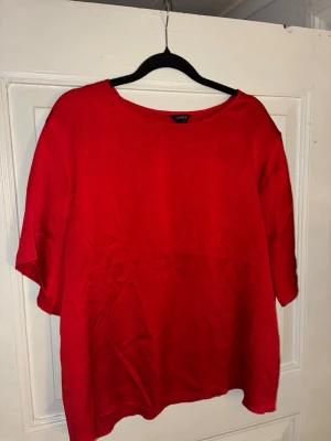 Röd satin blus från Lindex - Enkel och snygg röd satin blus från Lindex med lös passform och rund halsringning. Blusen har korta ärmar och är tillverkad i ett lätt och luftigt tyg, perfekt för en avslappnad stil.