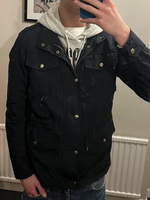 Svart feild jacka från Massimo Dutti - Säljer en svart feild jacka från Massimo Dutti med snygga guldiga knappar och dragkedja. Jackan har fyra stora fickor framtill och ett mönstrat innerfoder. Perfekt för dig som vill ha en stilren och praktisk jacka till vardags.