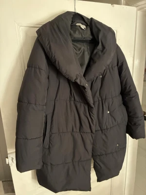 Svart pufferjacka från H&M, strl 38 - Säljer en svart pufferjacka från H&M i storlek 38. Jackan har en oversized krage, tryckknappar och två fickor på sidorna. Perfekt för kalla dagar med sin fluffiga och quiltade design. Enkel och stilren look som funkar till det mesta.