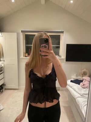Svart topp - Säljer en svart korsettopp med tunna axelband och volangdetaljer. Toppen har snörning framtill och är croppad med en luftig, lätt transparent känsla. Hör av er vid frågor💗💗