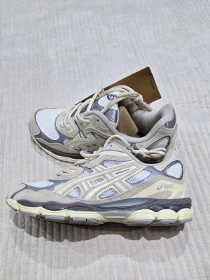 Asics sneakers i beige och grå mesh - Säljer ett par snygga Asics sneakers i beige, grå och vitt. Skorna har en chunky sula, meshpaneler för extra ventilation och detaljer i mocka. Klassisk Asics-logga på sidan och snörning framtill. Perfekta för dig som gillar stilrena och sportiga vibes.