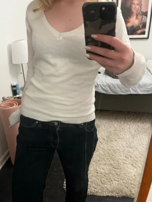 Vit v-ringad tröja - Säljer en stilren vit tröja med v-ringning och långa ärmar. Tröjan har ribbade muddar vid ärmslut och nederkant, vilket ger en snygg och enkel look. Perfekt att matcha med jeans eller kjol för en clean vibe.