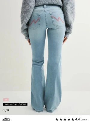 Ljusblå bootcut jeans från Nelly - De är dom med hål på knäna! Säljer ett par ljusblå bootcut jeans från Nelly med broderad detalj i rosa på bakfickorna. Jeansen har låg midja och är tillverkade i klassiskt denimtyg. Perfekta för dig som gillar en retroinspirerad look med extra vidd nedtill. 