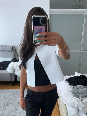 Vit kort kofta med guldlås - Säljer en stilren vit kofta från zara med kort ärm och en snygg guldig knapp upptill. Jackan är croppad och har en rak passform som ger en modern look. Perfekt att slänga över ett linne eller t-shirt för en clean och fräsch outfit. Går ej att köpa mer!💕