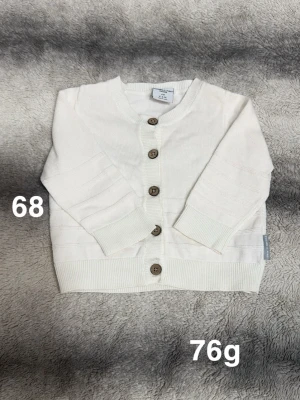 Vit kofta med knappar Polarn o pyret  - Söt vit kofta från Polarn o pyret i storlek 68. Koftan har långa ärmar, ribbade muddar och träfärgade knappar framtill. perfekt för lager-på-lager under kyligare dagar.🌸 Fint använt skick. Storlek 68