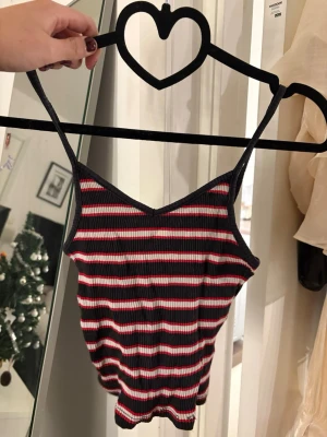 Randig ribbad linnetopp - Säljer en ribbad linnetopp med smala axelband och v-ringad hals. Toppen har ett randigt mönster i svart, vitt och rött. Perfekt för varma dagar eller att styla lager på lager. Tyvärr har jag klippt bort lappen vart den är i från samt storlek men det är en Xs-S och tror den är från newyorker.