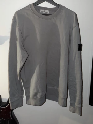 Grå sweatshirt från Stone Island - Säljer en stilren grå sweatshirt från Stone Island med klassisk patch på ärmen. Tröjan har rund halsringning, långa ärmar och ribbade muddar. Perfekt för dig som gillar clean streetwear och vill ha något enkelt men ändå fett. Inköpt för mindre än ett år sedan för 3000 kronor. Kan även konfirmera att tröjan är äkta med en bild på certilogon som tas privat.
