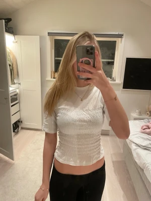 Vit croppad topp med smock - Säljer en vit croppad topp med smockad midja och korta ärmar. Toppen har en tight passform över kroppen och är tillverkad i ett mjukt och stretchigt material. Hör av er vid fler frågor