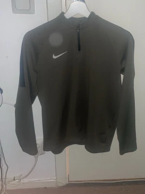 Svart Nike Dri-Fit träningströja XL - Nike Dri-Fit träningströja i svart med halv dragkedja och klassisk vit Nike-logga på bröstet. Tillverkad i ett lätt och funktionellt material som andas, perfekt för träning eller sport. Passar dig som gillar sportig och clean stil.