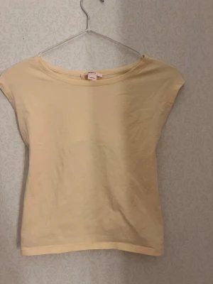 Gul topp med öppen rygg från Gina Tricot - Säljer en ljusgul topp från Gina Tricot i mjuk bomull. Toppen har ärmlös design, rund halsringning och en snygg öppen rygg med knyt längst ner. 