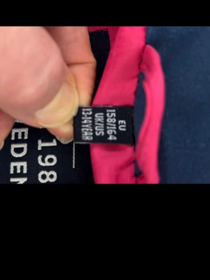 Rosa pufferjacka från Five Seasons - Snygg rosa pufferjacka från Five Seasons med vit dragkedja och fickor. Jackan har en mörkblå insida och huva, samt logga broderad på bröstet. Perfekt för kalla dagar och har en modern, ungdomlig look.