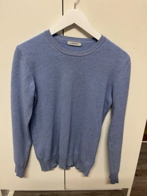 Ljusblå kashmir tröja J.Lindeberg - En stilren ljusblå stickad tröja från J.Lindeberg i storlek M. Tröjan har rund halsringning, ribbade muddar och är långärmad. Den är i en Kashmir blend med 70% Kashmir och 30% merino ull.