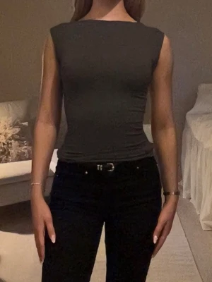 Mörkgrå ärmlös topp i stretchigt material - Säljer en mörkgrå, tight och ärmlös topp med rund halsringning. Toppen är figurnära och har en enkel, stilren design utan synliga detaljer. 