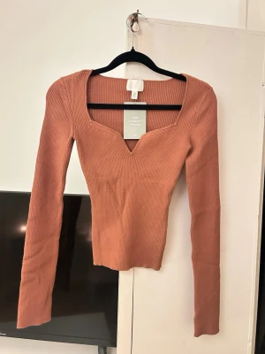 Rostbrun ribbad topp från H&M - Säljer en ribbad topp i rostbrun färg från H&M. Toppen har lång ärm, v-ringad halsringning med snygg kant och är figurnära i modellen. Materialet är mjukt och stretchigt, perfekt till jeans eller kjol.