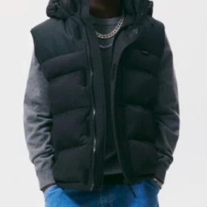 Zara väst herr  - Snygg svart dunväst med huva och dragkedja framtill. Västen har en puffig, quiltad design och är perfekt att bära över en hoodie eller tröja. Passar till många olika stilar och håller dig varm under kyliga dagar.priset kan diskuteras vid snabb affär. 