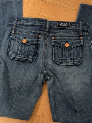 Rock & Republic blå jeans med fickor - Säljer dessa super snygga blå jeans från Rock & Republic med fickor med lock och kopparfärgade knappar bak. Jeansen har världens snyggaste tvätt. Jeansen har klassisk femficksdesign och är tillverkade i 99% bomull och 1% elastan för lite stretch.