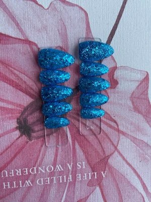 Blå glittriga lösnaglar i mandelform - Säljer ett set med lösnaglar i mandelform, täckta av blått glitter som verkligen poppar. Naglarna är i gele och har en snygg, glittrig finish som drar blickarna till sig. Perfekt för dig som vill ha något extra till naglarna.