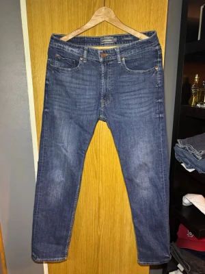 Blå jeans från Dressmann Regular Fit - Säljer ett par klassiska blå jeans från Dressmann i modellen Regular Fit. Jeansen har fem fickor, normal passform och raka ben. Tillverkade i slitstarkt denim. Perfekta till vardagslooken.
