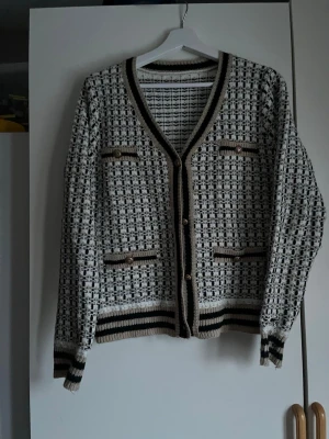 Beige och svart rutig kofta med guldknappar - Säljer en rutig kofta i beige, svart och vitt med guldknappar framtill. Använder både stängd men även som kofta. Har haft den 2 gången så den är väldigt ny. 