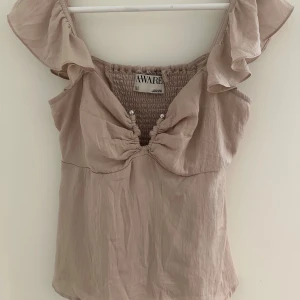 Gammel rosa blus med volang från AWARE - Säljer en gammel rosa blus från AWARE i storlek S. Toppen har volangdetaljer på axelbanden, smockad rygg med v-ringning. Materialet är mjukt och lätt, perfekt för varma dagar. Supersöt och trendig modell! Användts väldigt några gånger då den är för lite för liten för mig. 