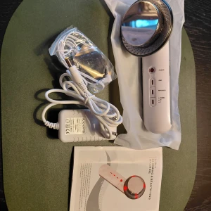 Ny Skincare Options massage/ Slimming/EMS - Slimming & Beautifying Machine med vit plastkropp och rund metallplatta. Levereras med strömadapter, sladd och manual. Perfekt för hudvård och ansiktsbehandlingar hemma. Maskinen har flera inställningar och LED-indikatorer. 3 in 1 EMS massage / Slimming. Finns flera lägen och massage/Slimming olja Mitt pris: 200:-