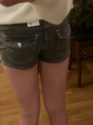 Grå denimshorts med fickdetaljer - Säljer ett par gråa denimshorts från 157 med snygg tvättad look. Shortsen har snygga bakfickor med lock och knapp, samt klassiska framfickor. Modellen är mellan Lågmidjade och medium och har en normal passform. Perfekta till sommaren för en avslappnad vibe. Upplever att storleken inte riktigt stämmer då jag igentligen har 164  i barnstorlek. Aldrig använda och lapparna kvar. Pris går att diskuteras!