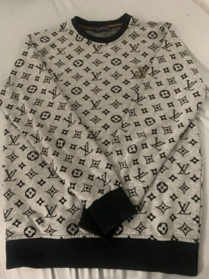 Grå Louis Vuitton sweatshirt M - Säljer en grå sweatshirt från Louis Vuitton i storlek M. Tröjan har svartvitt monogrammönster över hela, ribbade muddar och en snygg LV-detalj i guld på bröstet. Perfekt för dig som vill ha en statement piece i garderoben. Jag säljer en lv tröja som jag fick i present förra året men jag vill sälja den, tröjan köptes i Tyskland.  Storlek M  Tröjan har en QR kod som leder till lv webbsidan. 749 euro ny pris.