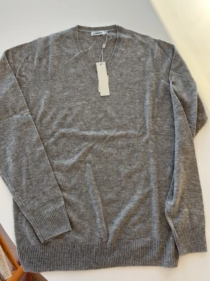 Grå v-ringad tröja från J.Lindeberg - Snygg grå v-ringad tröja från J.Lindeberg i mjuk ullmix. Klassisk passform med ribbade muddar vid ärmslut och nederkant. Perfekt till lager på lager och funkar året runt. Enkel och stilren design som passar till det mesta.