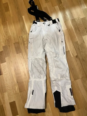 Vita skidbyxor från Icepeak med hängslen - Säljer ett par vita skidbyxor från Icepeak med svarta detaljer och justerbara hängslen. Byxorna är i ett väldigt bra skick 