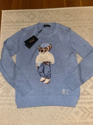 Polo Ralph Lauren Bear tröja ljusblå – Ny med tag – Herr S/XS - Säljer denna blåa Polo Ralph Lauren tröja med en björn som design. Den är storlek S men kan passa XS. Skulle säga att den är liten i storlek.