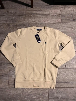 Polo Ralph Lauren sweatshirt  - Polo Ralph Lauren sweatshirt i beige med klassisk broderad logga på bröstet. Tidlös modell i mjukt och bekvämt material. Fick den som gåva från min far när han var i Frankrike 🇫🇷 men tyvvär var den för stor på mig, aldrig använd – originaltag kvar.                                                           Perfekt nu till våren 🔥
