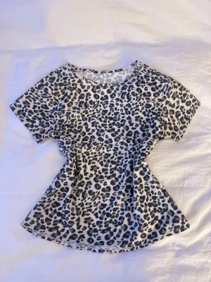 Leopardmönstrad kortärmad topp - Säljer en snygg topp med leopardmönster i beige, svart och bruna toner. Modellen är kortärmad med rund hals och lätt figurnära passform. Perfekt för dig som vill sticka ut med ett djuriskt print. Materialet känns mjukt och följsamt mot huden.