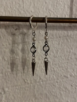 Snygga silverfärgade spikeörhängen - Unika örhängen i silverfärg med små pärlor, en rund detalj och en spetsig spike längst ner. Perfekta för dig som vill ha en edgy och cool accessoar till din outfit. Lätta att bära och passar till många olika stilar.