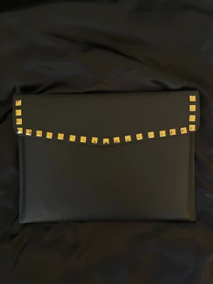 Datorfodral med guld nitar i läder imitation  - Rea - endast 199 kr (ord. pris 249 kr)! Stilrent datorfodral tillverkat av veganskt läder i vattentätt material. Fodralet stängs med knapp. Fodralet skyddar din dator effektivt samtidigt som det ger din outfit en extra touch. ⚜️ Storlek: 34 × 25 cm – passar svarta HP Chromebooks och andra datorer i liknande storlek. 1-3 arbetsdagar leverans 📦 