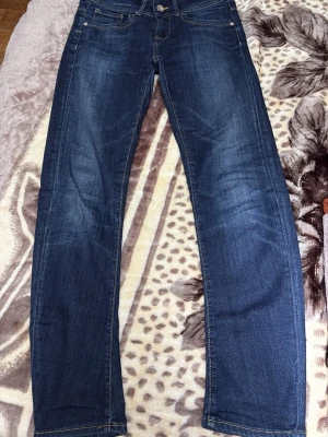 Mörkblå raka jeans W28 L30 - Snygga mörkblå jeans med klassisk rak passform och fem fickor. Jeansen har kontrastsömmar och är tillverkade i slitstarkt denimtyg. Perfekt för dig som gillar en enkel och tidlös stil. Storlek W28 L30.