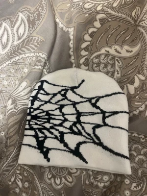 Vit mössa med svart spindelnätsmönster - Säljer en vit mössa med ett coolt svart spindelnätsmönster på framsidan och baksidan . Perfekt för dig som gillar unika accessoarer med lite edge. Mössan är mjuk och stretchig, passar de flesta huvudstorlekar.