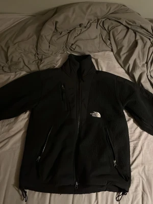 The North Face Fleecejacka - En skön och fin jacka från märket The North Face. Jackan svart med vita detaljer och dragkedjor. Perfekt för dig som söker en varm jacka för hela året om!