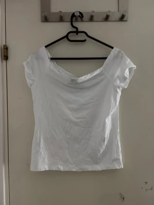 Vit offshoulder topp från Vero moda - Säljer en enkel och stilren vit topp från Vero moda med offshoulder-design och korta ärmar. Toppen har en mjuk, något stretchig känsla och är tillverkad i bomullsmix. Perfekt till jeans eller kjol för en clean look.