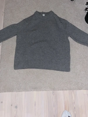 Grå stickad tröja från Arket - En klassisk grå stickad tröja från Arket i storlek M. Tröjan har rund halsringning, ribbade muddar och är långärmad. Perfekt för lager-på-lager under kyliga dagar. Enkel och stilren design som funkar till det mesta.