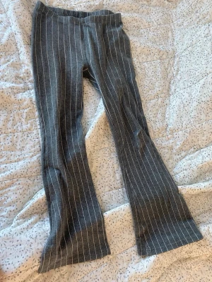 Grå randiga bootcut-byxor XOXO friends - Grå bootcut-byxor från XOXO friends med vita vertikala ränder. Byxorna har en mjuk och stretchig känsla, elastisk midja och utsvängda ben. 