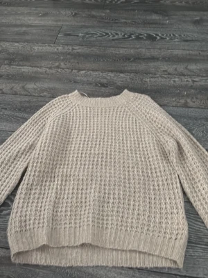 Beige stickad tröja från 157 - Mysig beige stickad tröja från 157 i storlek S. Tröjan har ett grovt stickat mönster, rund halsringning och ribbade muddar vid ärmslut och nederkant. Perfekt för kyliga dagar och enkel att matcha med jeans eller kjol.