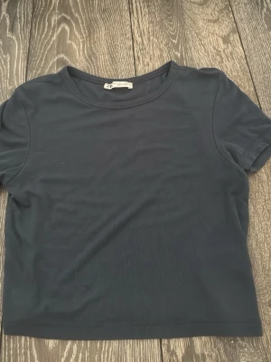 Mörkblå t-shirt från Zara - En enkel och stilren mörkblå t-shirt från Zara med rund halsringning och korta ärmar. Tillverkad i mjuk bomull som känns skön mot huden. Perfekt basplagg att matcha med allt i garderoben. Passformen är att den är kort 