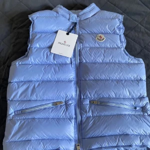 Ljusblå M*ncl*r - Snygg ljusblå dunväst från Moncler. Västen har två dragkedjefickor framtill, diskret logga på bröstet och stängs med dragkedja. Perfekt för lager-på-lager och ger en clean look. Pris kan diskuteras