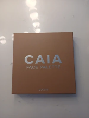 CAIA Face Palette Classy - Säljer en CAIA Face Palette Classy med fyra olika puder: contour, blush, bronzer och highlighter. Paletten har en snygg beige/brun förpackning med spegel och silvrig text. Pudren har varma, naturliga toner och highlightern har ett skimrande mönster. Perfekt för att skapa en fräsch look.