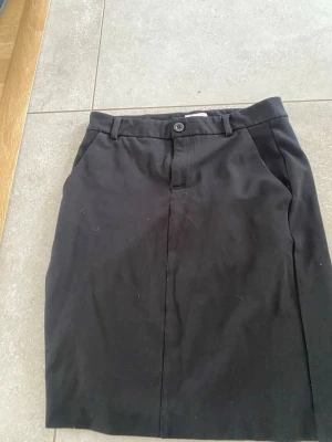 Svart pennkjol från Signal - Klassisk svart pennkjol från Signal i storlek 34. Kjolen har hällor för bälte, knapp och dragkedja fram samt fickor på sidorna och dekorfickor bak. Enkel och stilren design som passar till många olika looks.