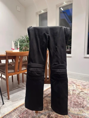 Snygga skidöverdrags från McKinley - Säljer ett par svarta skidöverdrag från McKinley med förstärkta partier över knäna och dragkedjor vid bensluten som för de enkelt med pjäxor. Byxorna har justerbar midja med kardborre, två dragkedjeförsedda fickor och är fodrade för extra värme. Perfekta för kalla dagar i backen. Nya 1200kr