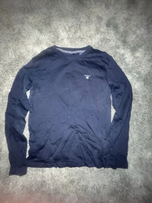 Mörkblå långärmad tröja från GANT - Säljer en mörkblå långärmad tröja från GANT med klassisk rund hals och diskret logga broderad på bröstet. Tillverkad i mjuk bomull som känns skön mot huden. Perfekt till skolan eller chill dagar.